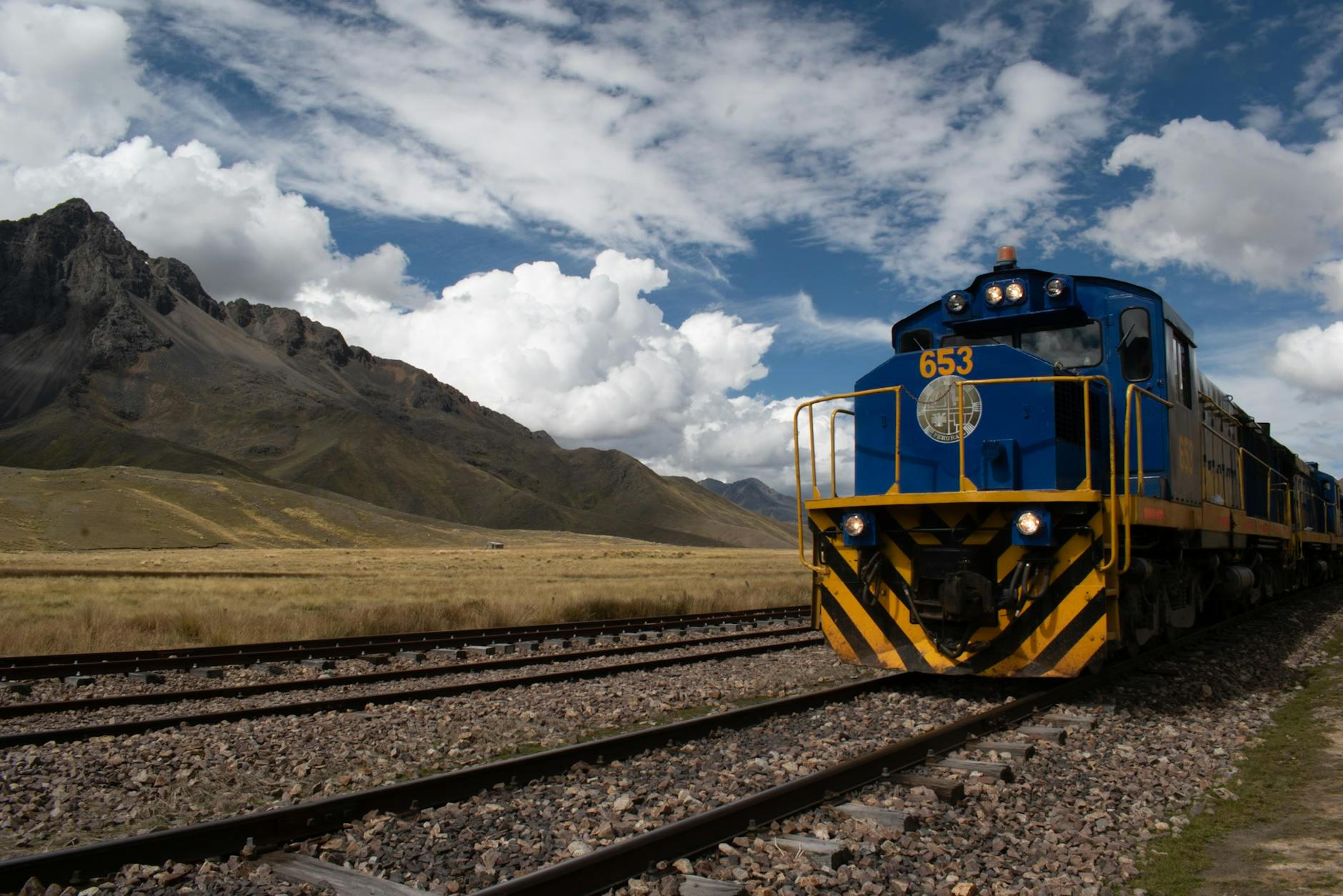 Niebieski pociąg jedzie górską trasą kolejową pod pochmurnym niebem