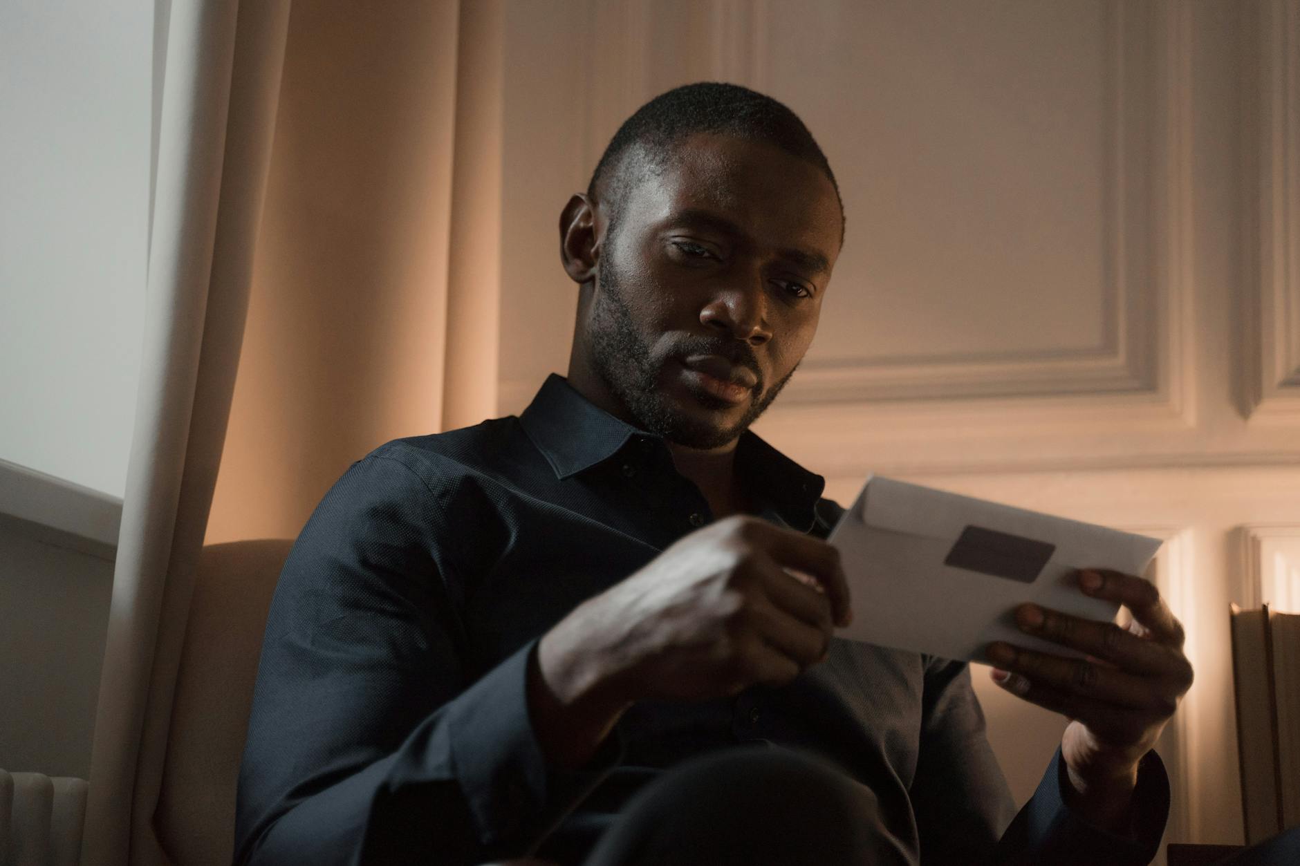 Mężczyzna z wąsem uważnie czyta list w ciepło oświetlonym pokoju