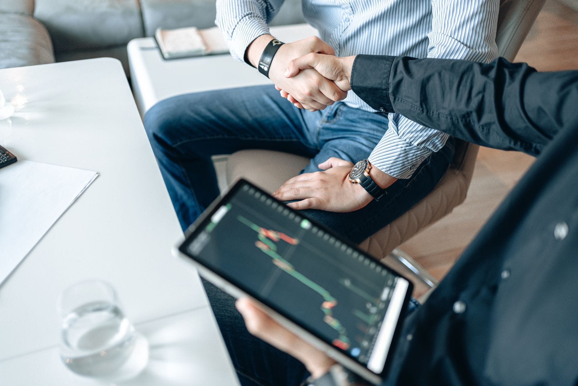 Biznesmeni podają sobie rękę nad tabletem z wykresami finansowymi