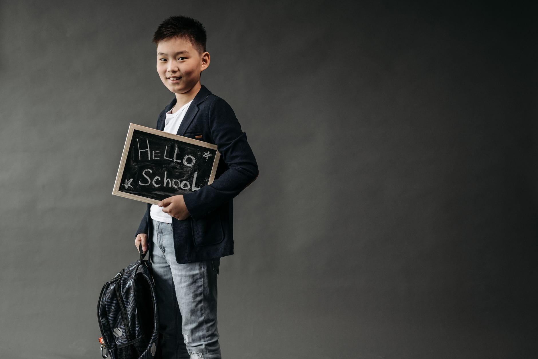 Chłopiec z plecakiem trzyma tabliczkę z napisem Hello School Chłopiec z plecakiem trzyma tabliczkę z napisem Hello School