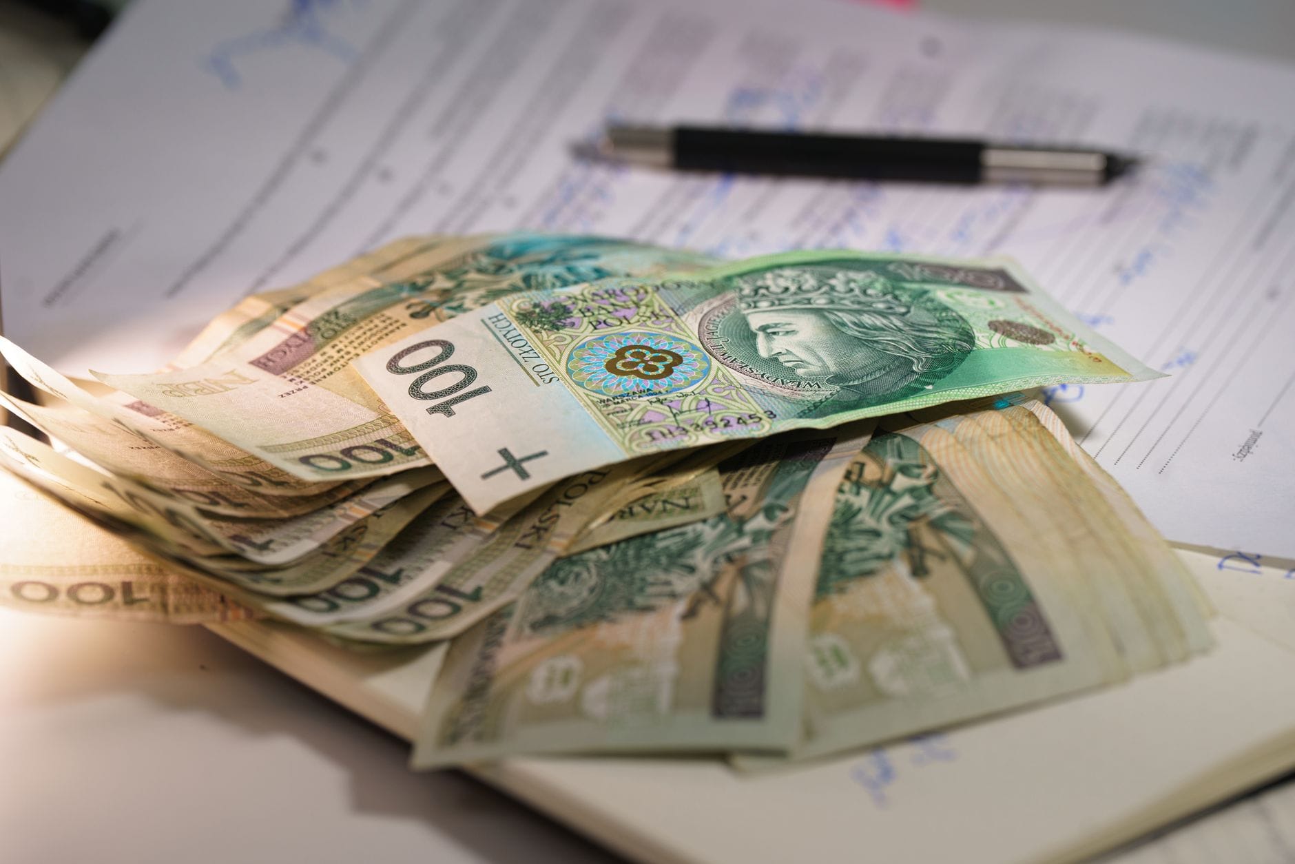 Plik banknotów złotych na dokumentach finansowych z długopisem