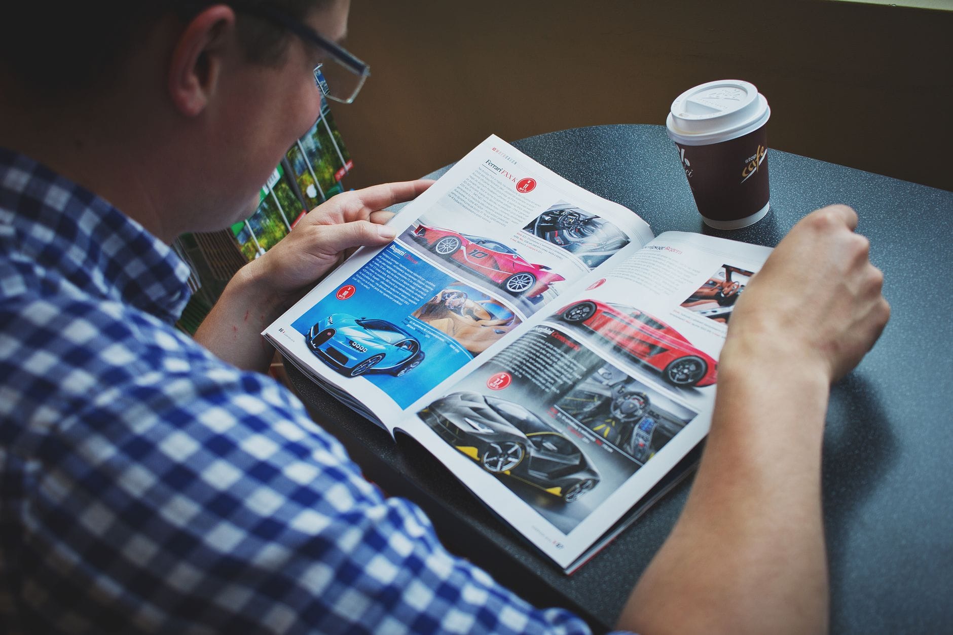 Najciekawsze książki o motoryzacji dla początkujących i zaawansowanych pasjonatów aut sportowych Mężczyzna czyta magazyn motoryzacyjny i pije kawę przy stoliku