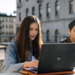 Studenci pracujący przy laptopie przed historycznym budynkiem uczelni