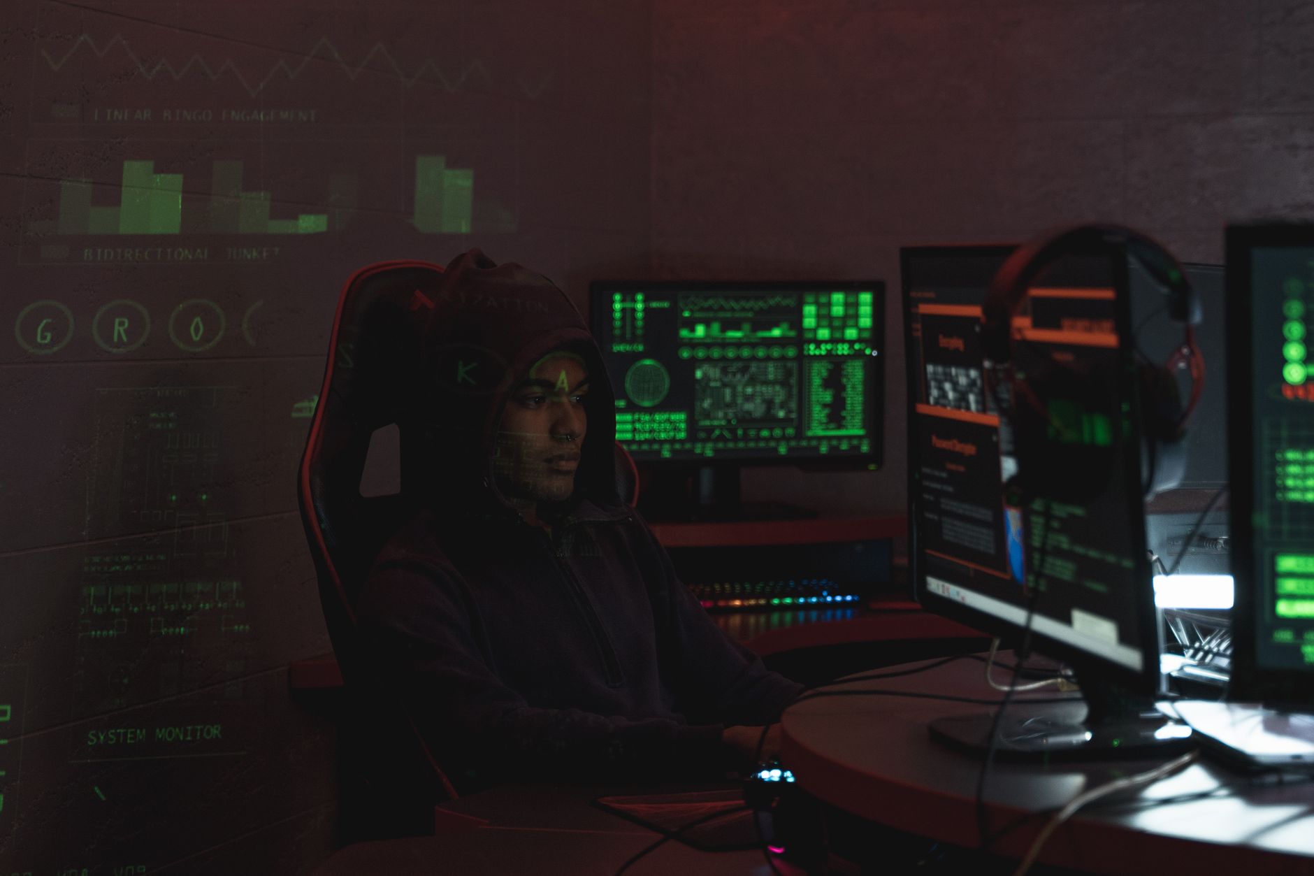 Mężczyzna w czarnej bluzie pracuje przy kilku monitorach nad cyberbezpieczeństwe