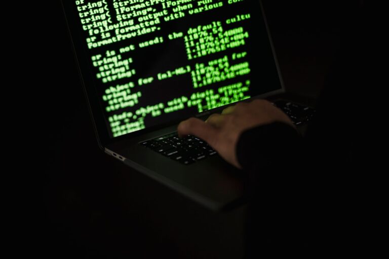 Osoba wpisująca kod na netbooku w ciemnym pomieszczeniu